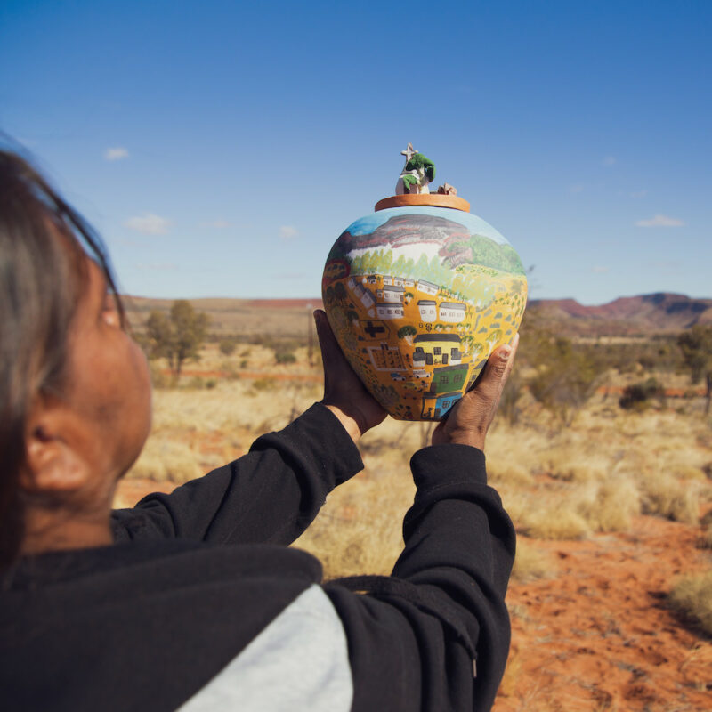 A Hermannsburg Potters artist holding her finished artwork. On our Palm Valley Tour. Red Centre tours, Australia.