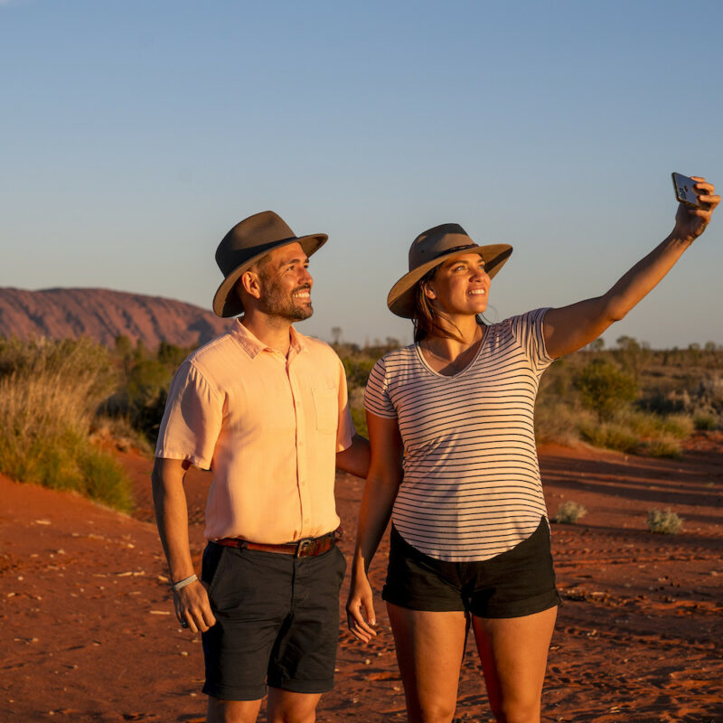 Real Aussie Adventures, Small Group Adventure Tours Australia. Couple taking a selfie with Uluru in the background on our Uluru tour outback camping adventures. 5 day red centre tour